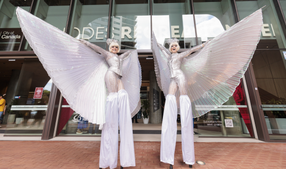 Stiltwalkers in glittery costume in front of Rhodes Recreation Centre
